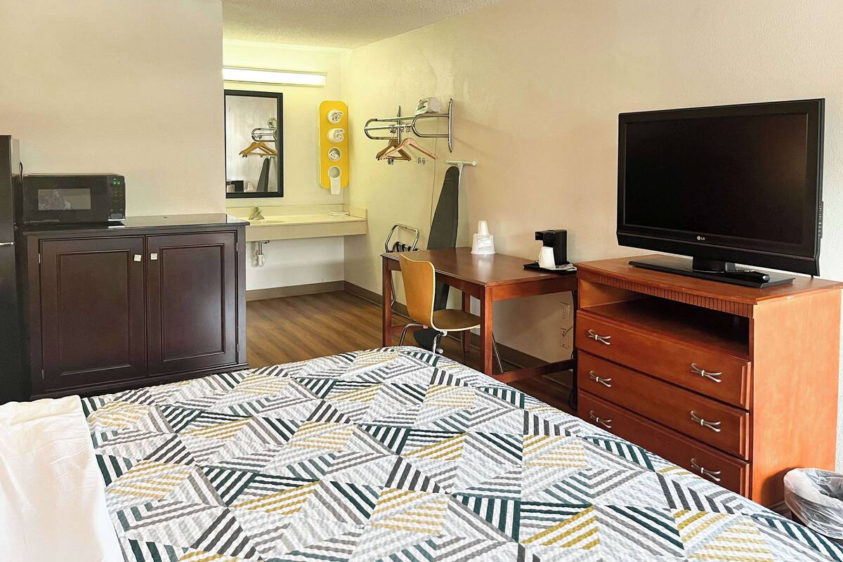 A hotel room with a bed, a desk, a television, a microwave, and a mirror.