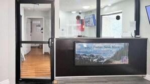 A reception area with a glass door leading to a hallway, a desk with a promotional poster, and a TV mounted on the wall. - Studio 6 Suites Dayton, Oh - Englewood (Englewood)
