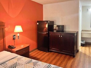 A hotel room with a bed, a desk with a lamp, a refrigerator, a microwave, and a cabinet. - Studio 6 Suites Dayton, Oh - Englewood (Englewood)