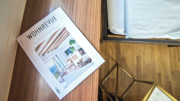 A magazine on a wooden floor with a bed in the background. - Tilia Apartments (Uster)