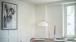A dining area with a round table, red chairs, a framed artwork on the wall, and a floor lamp. - Tilia Apartments (Uster)