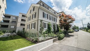 A modern two-story residential building with a well-maintained lawn and garden. - Tilia Apartments (Uster)