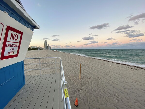 A beach with a lifeguard sign, a blue building, and a clear sky.