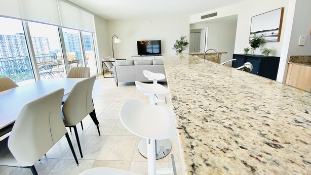 A modern apartment with a dining area, kitchen, living room, and large windows offering a city view. - The Javiera Beach Condo! 3BR/2BA in Sunny Isles Beach (Sunny Isles Beach)