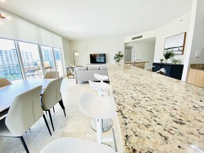 A modern apartment with a dining area, kitchen, living room, and large windows offering a city view.