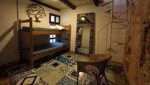 Una habitación con una cama litera, suelo estampado, una silla de mimbre y un mural de un árbol, además de una escalera de caracol.