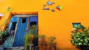 A vibrant orange building with a blue door, potted plants, and decorative fish on the wall.
