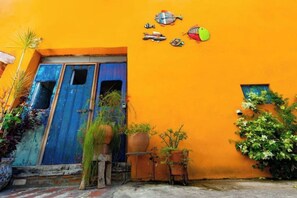 A vibrant orange building with a blue door, potted plants, and decorative fish on the wall.