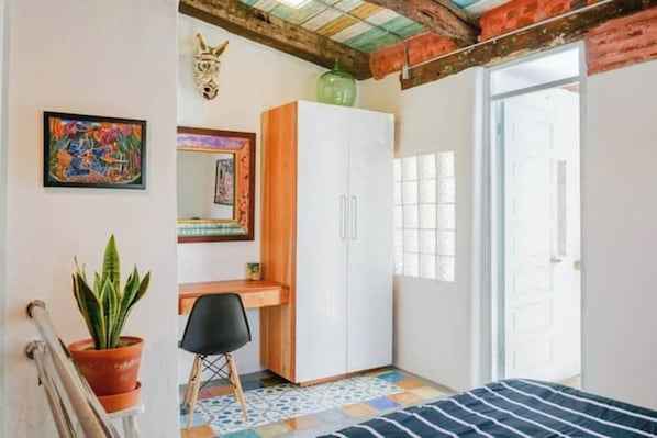 Un dormitorio con cama, escritorio, armario, planta en maceta y espejo.