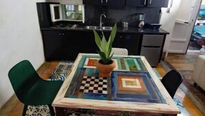 A compact kitchen with dark cabinets, a microwave, and a sink. A table with a patterned tablecloth and a potted plant is in the foreground.