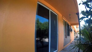 A building with a large sliding glass door, a tiled walkway, and a small outdoor area with a plant. - Apartamento #1-1 Casalaspalmas Puntademita (Punta de Mita)