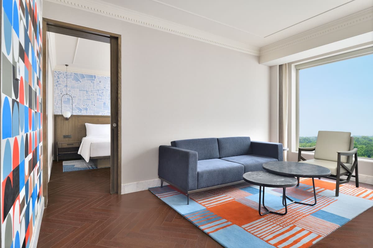 A modern hotel room with a sofa, a small round table, and a view of the outdoors.