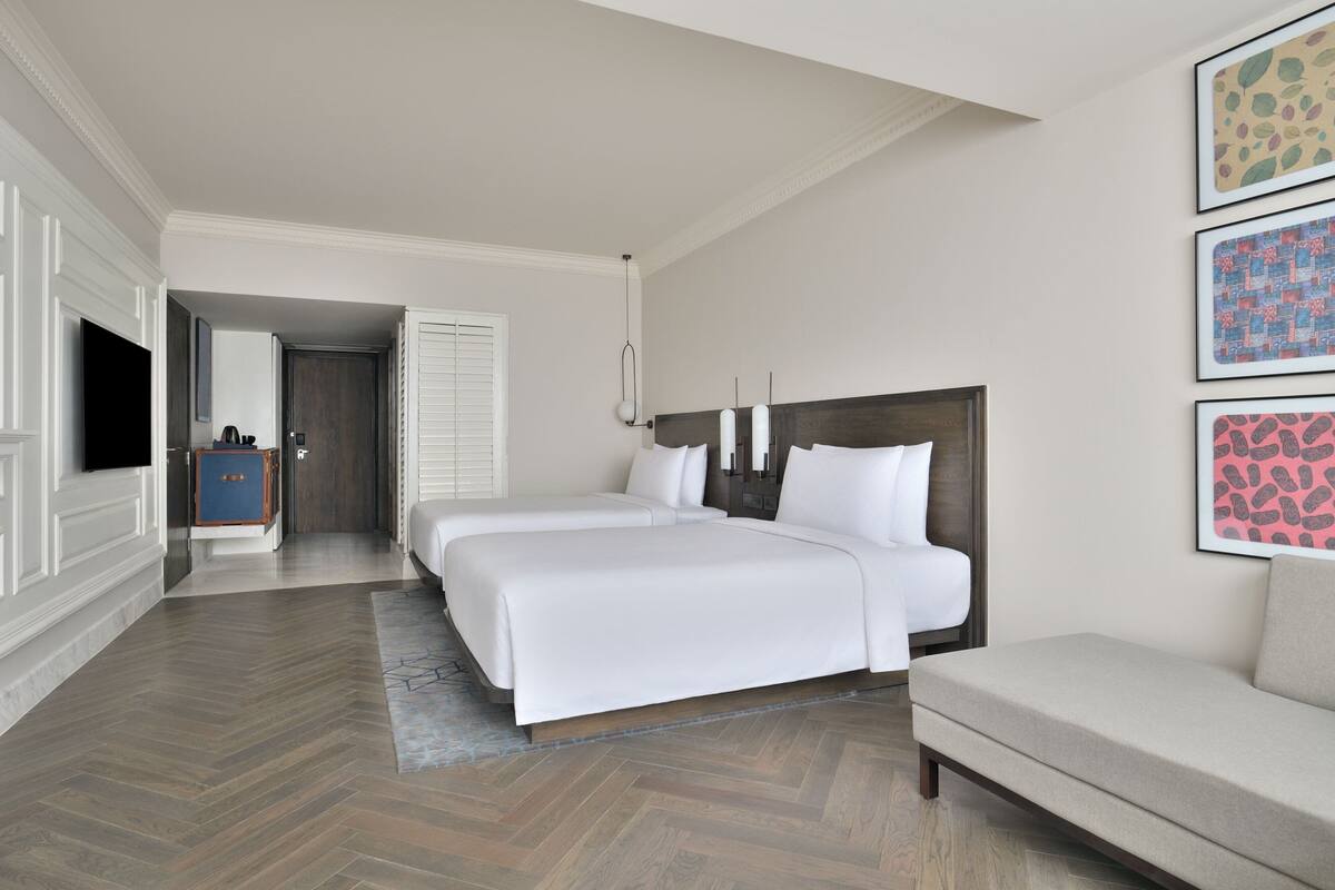 A hotel room with two beds, a sofa, a TV, and artwork on the walls.