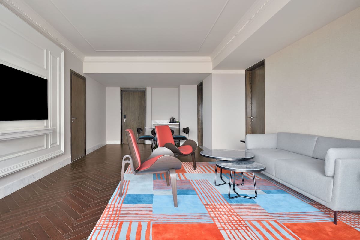 A modern living room with a sofa, a red and gray chair, a small round table, and a colorful rug.