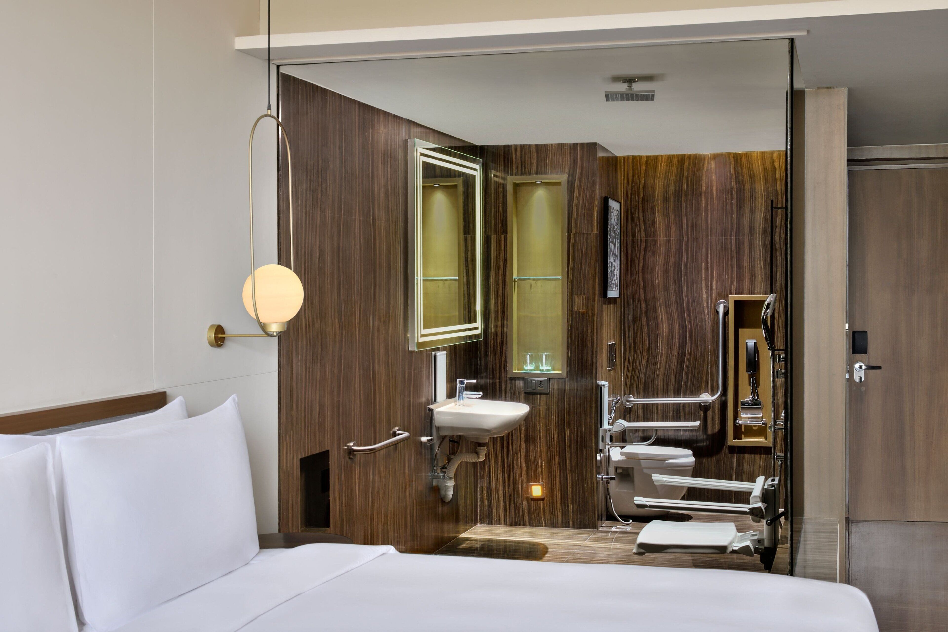 Habitación de hotel con cama, mesita de noche, espejo en la pared, lavabo y zona de ducha.