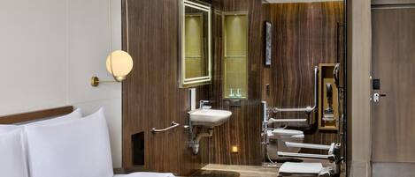Habitación de hotel con cama, mesita de noche, espejo en la pared, lavabo y zona de ducha.