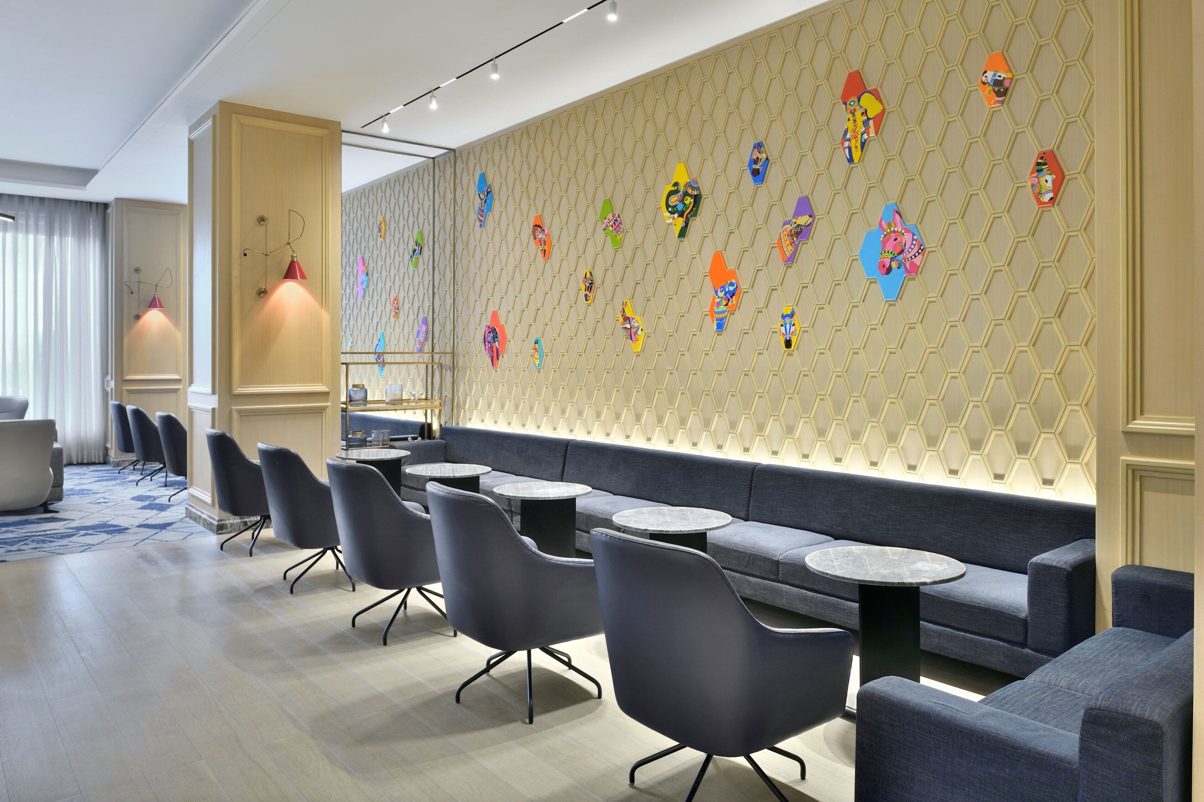 A modern lounge area with seating and tables, a patterned wall, and pendant lighting.