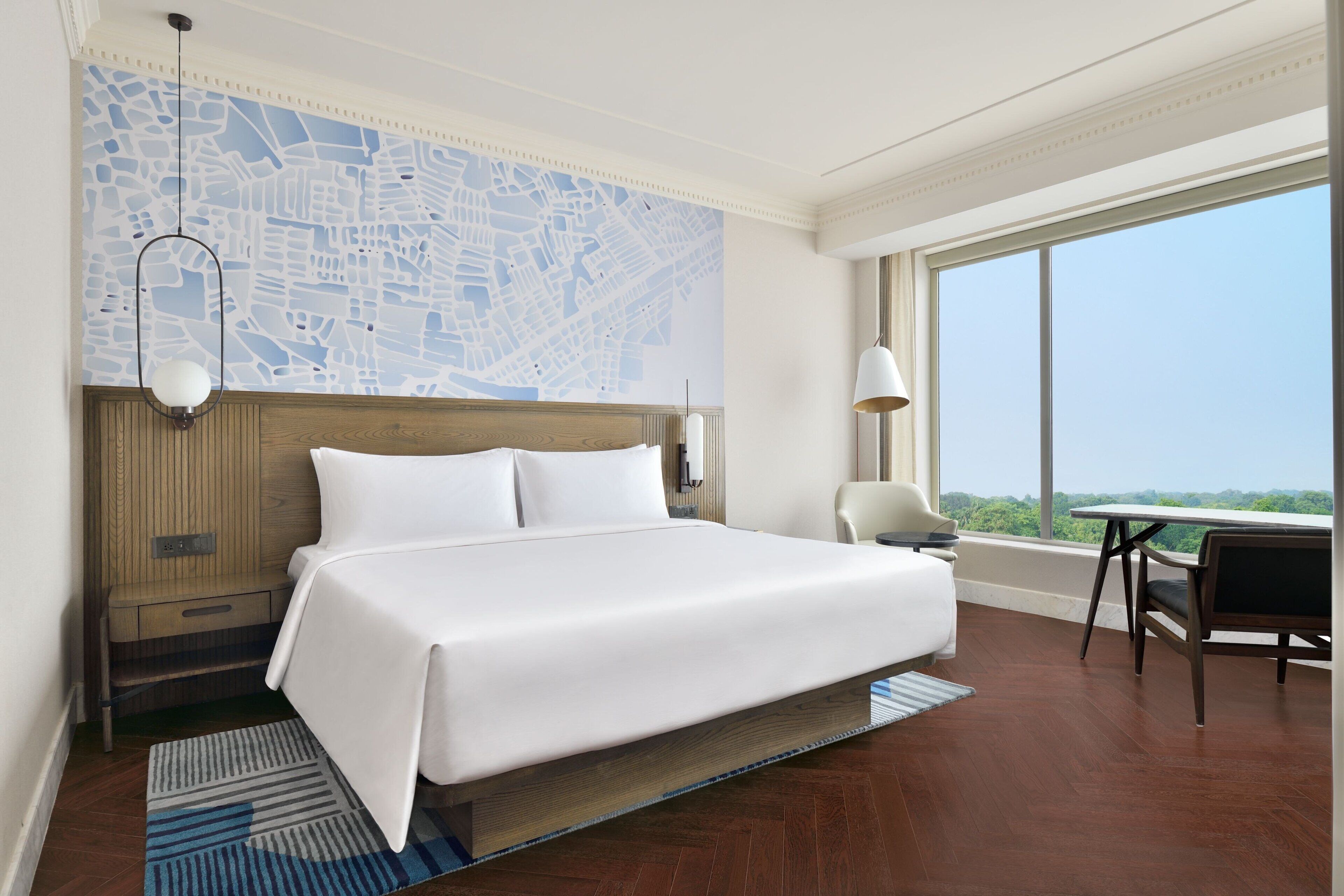 Habitación de hotel con una cama grande, un cuadro con vista a la ciudad, una mesa de comedor y vistas al exterior.