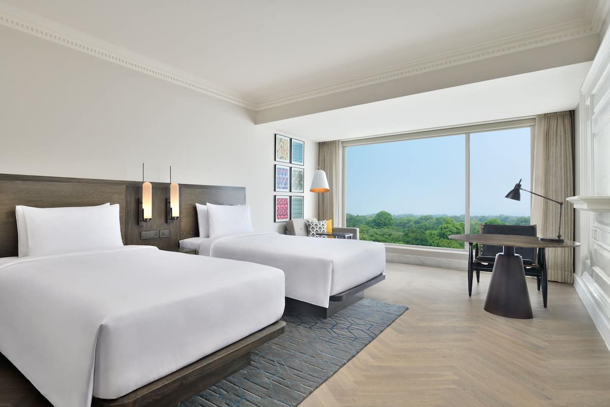 A hotel room with two beds, a desk, and a view of the outdoors.