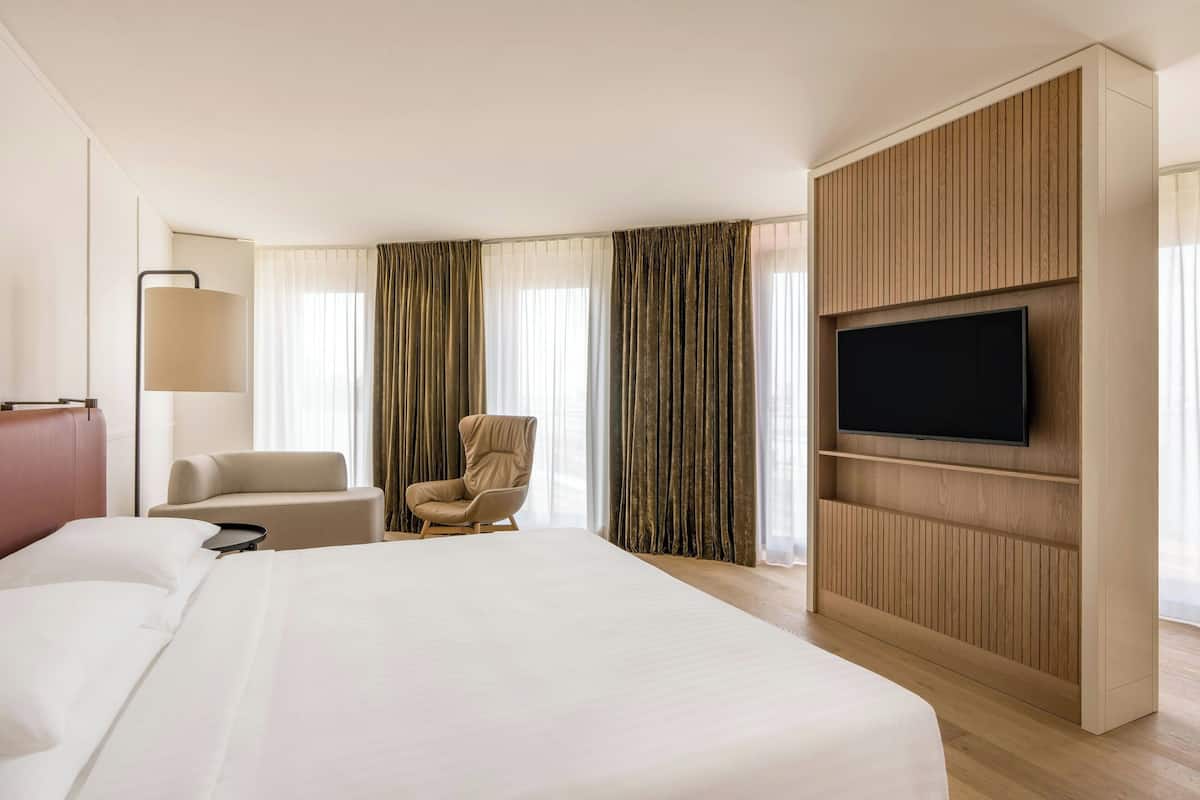 Una habitación de hotel con una cama grande, un televisor montado en la pared, una silla y un escritorio.