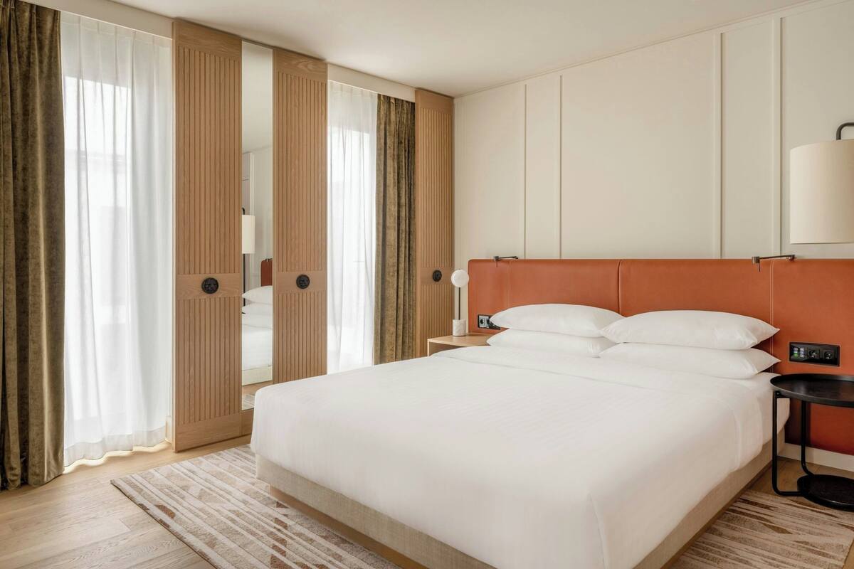 Una habitación de hotel con una cama grande, una mesita de noche, una lámpara y un armario.