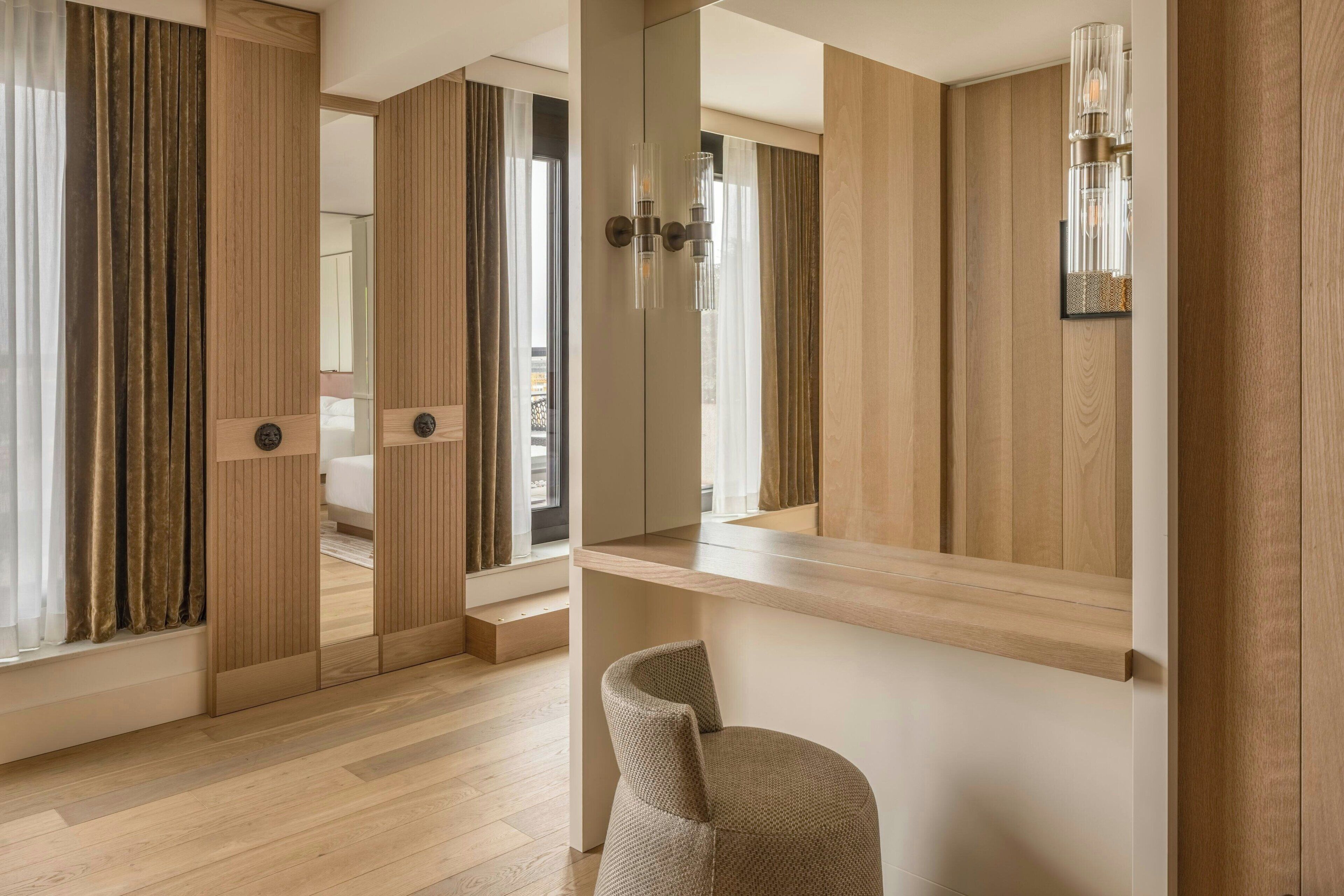 A modern hotel room with a wooden floor, a large mirror, and a wooden wardrobe.
