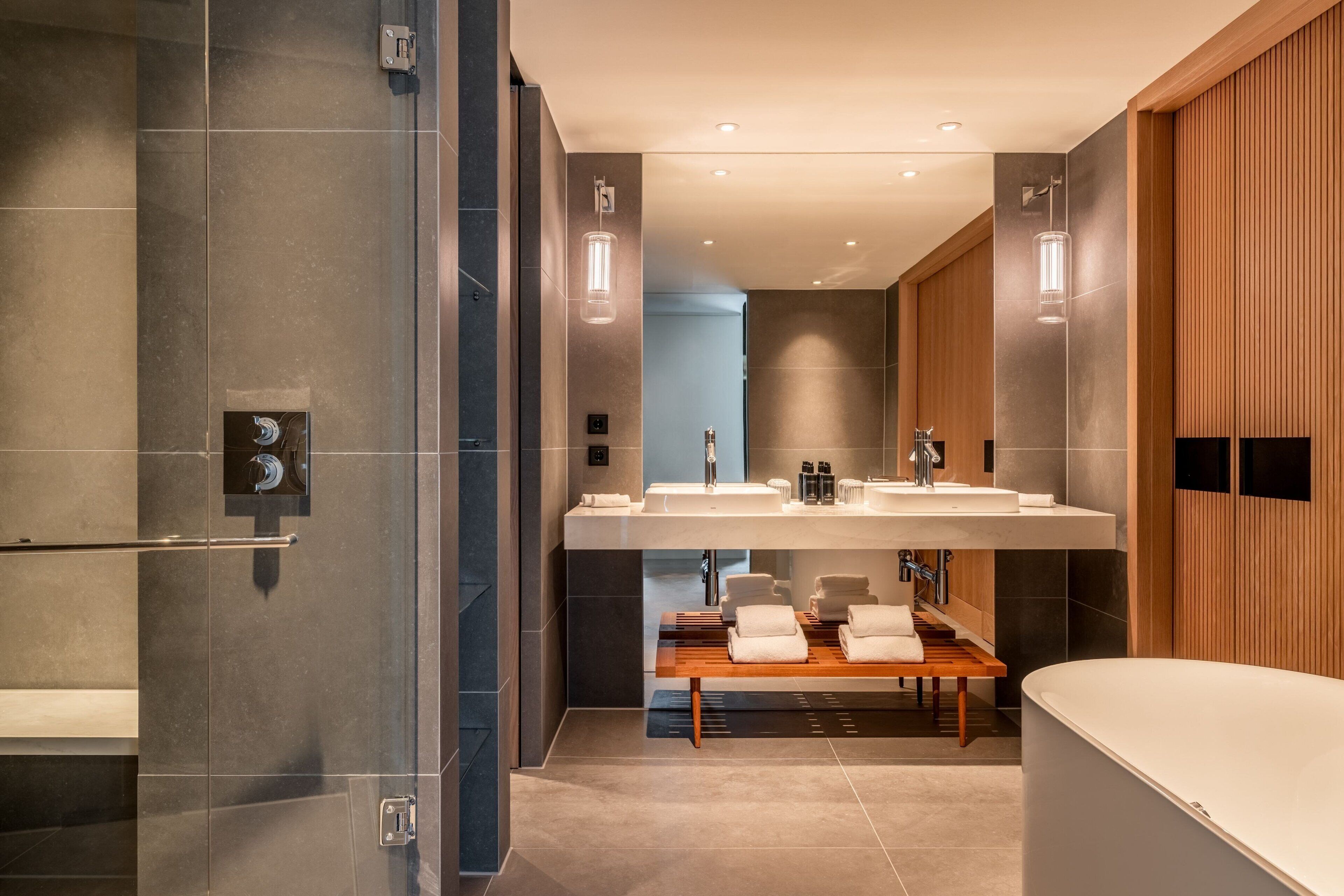 A modern bathroom with a glass shower enclosure, a wooden bench, and a large bathtub.