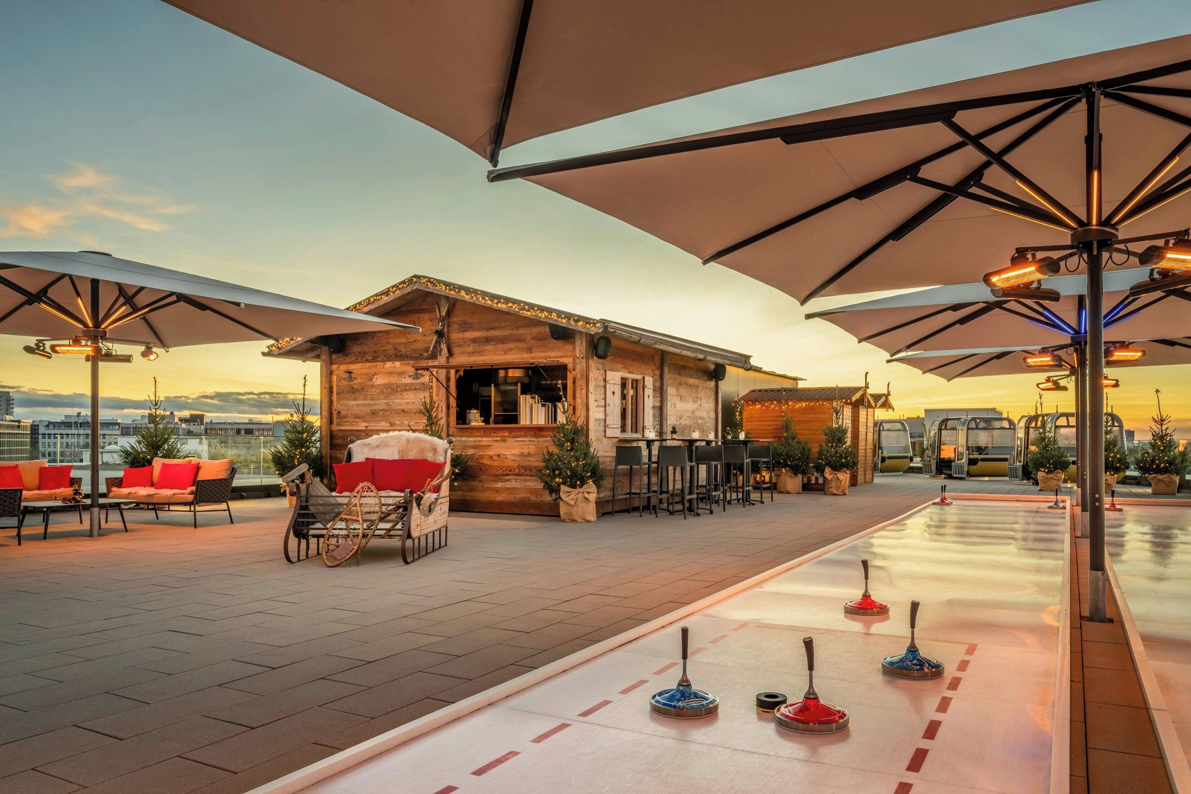 A rooftop terrace with outdoor seating, a bar area, and shuffleboard tables.