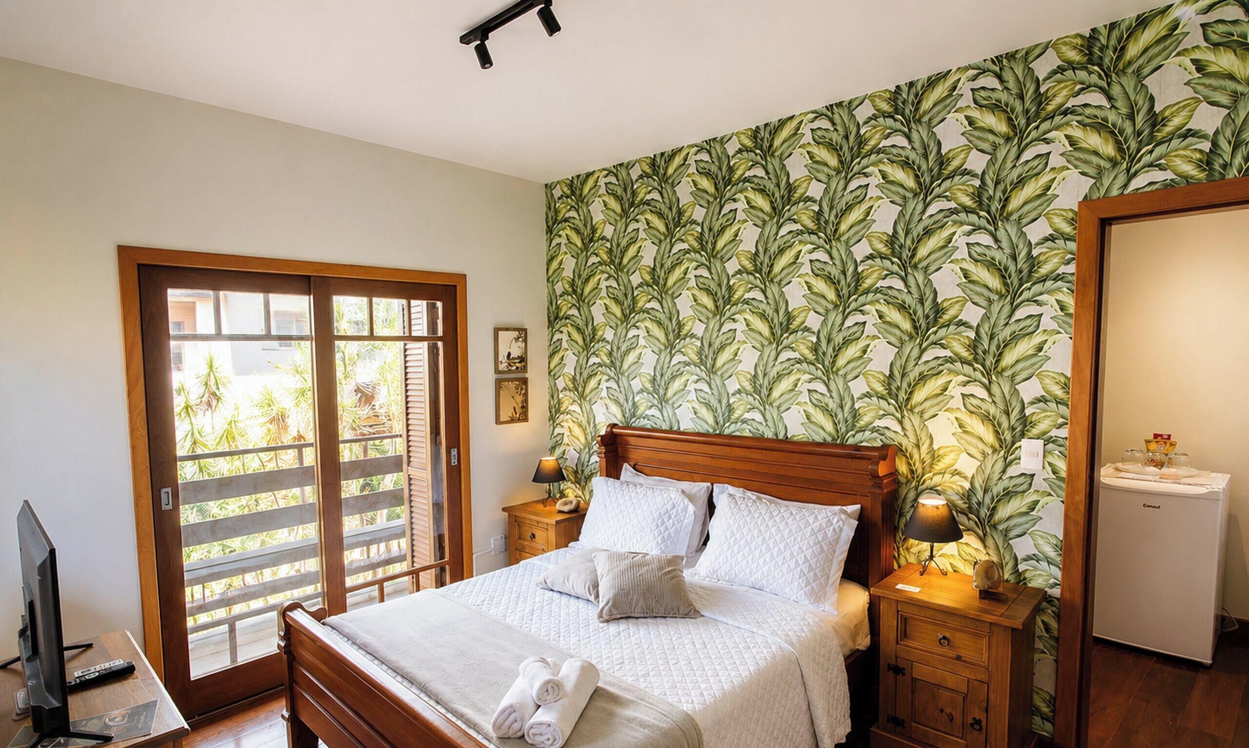 A bedroom with a bed, wooden headboard, bedside tables with lamps, a television, and a view through a sliding door to an outdoor area.