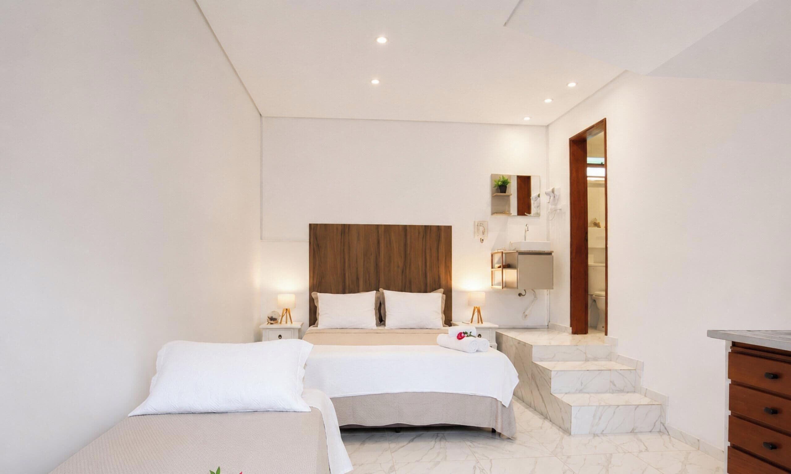 A modern bedroom with a large bed, a smaller bed, and a bathroom with a mirror and sink.