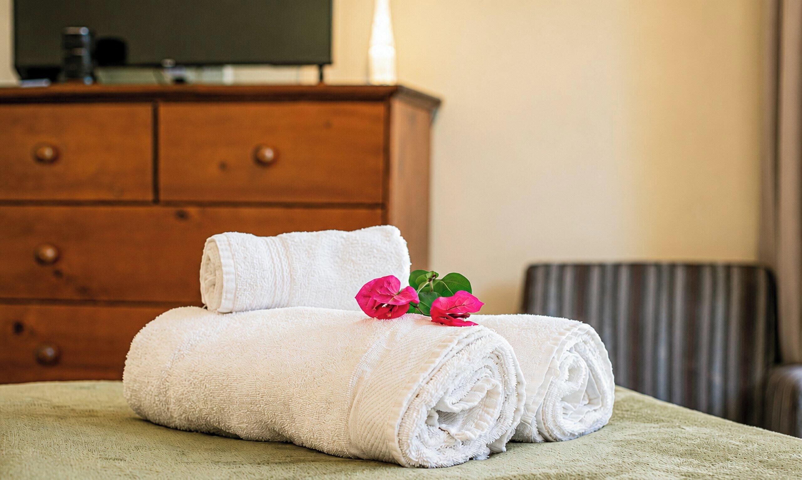 A neatly made bed with rolled white towels and a pink flower on a green bedspread.