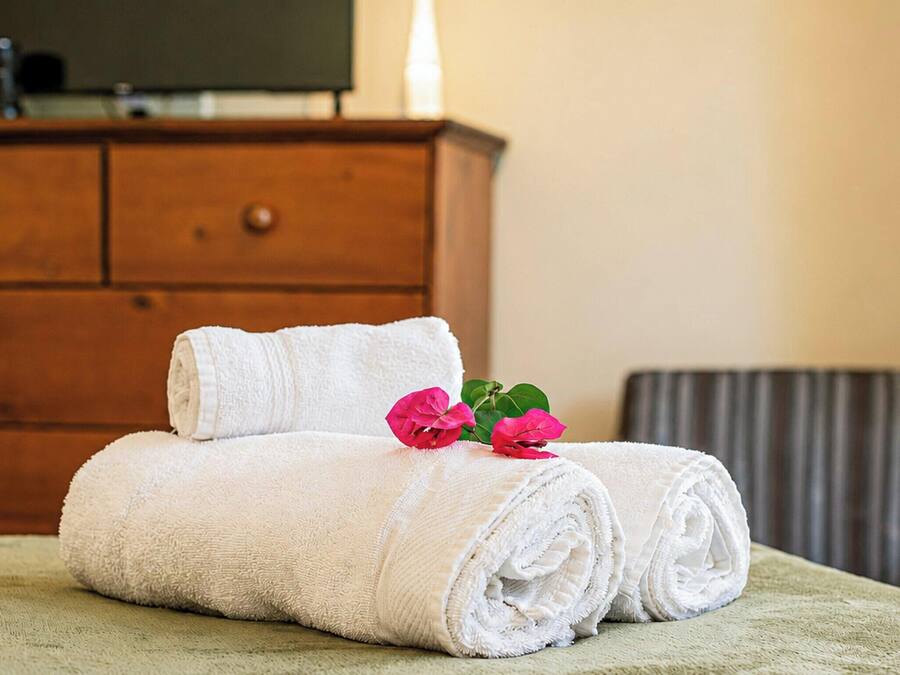 A neatly made bed with rolled white towels and a pink flower on a green bedspread.
