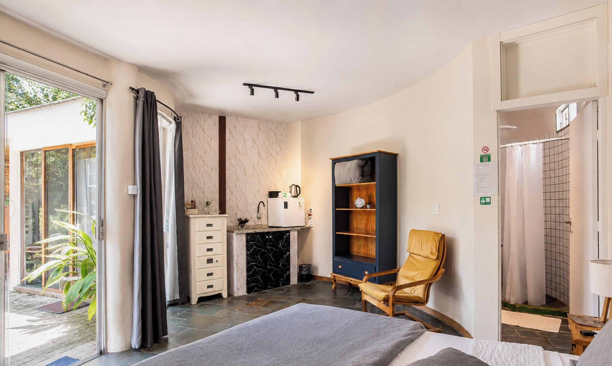 A bedroom with a bed, a wooden chair, a wardrobe, a sink, and a shower.