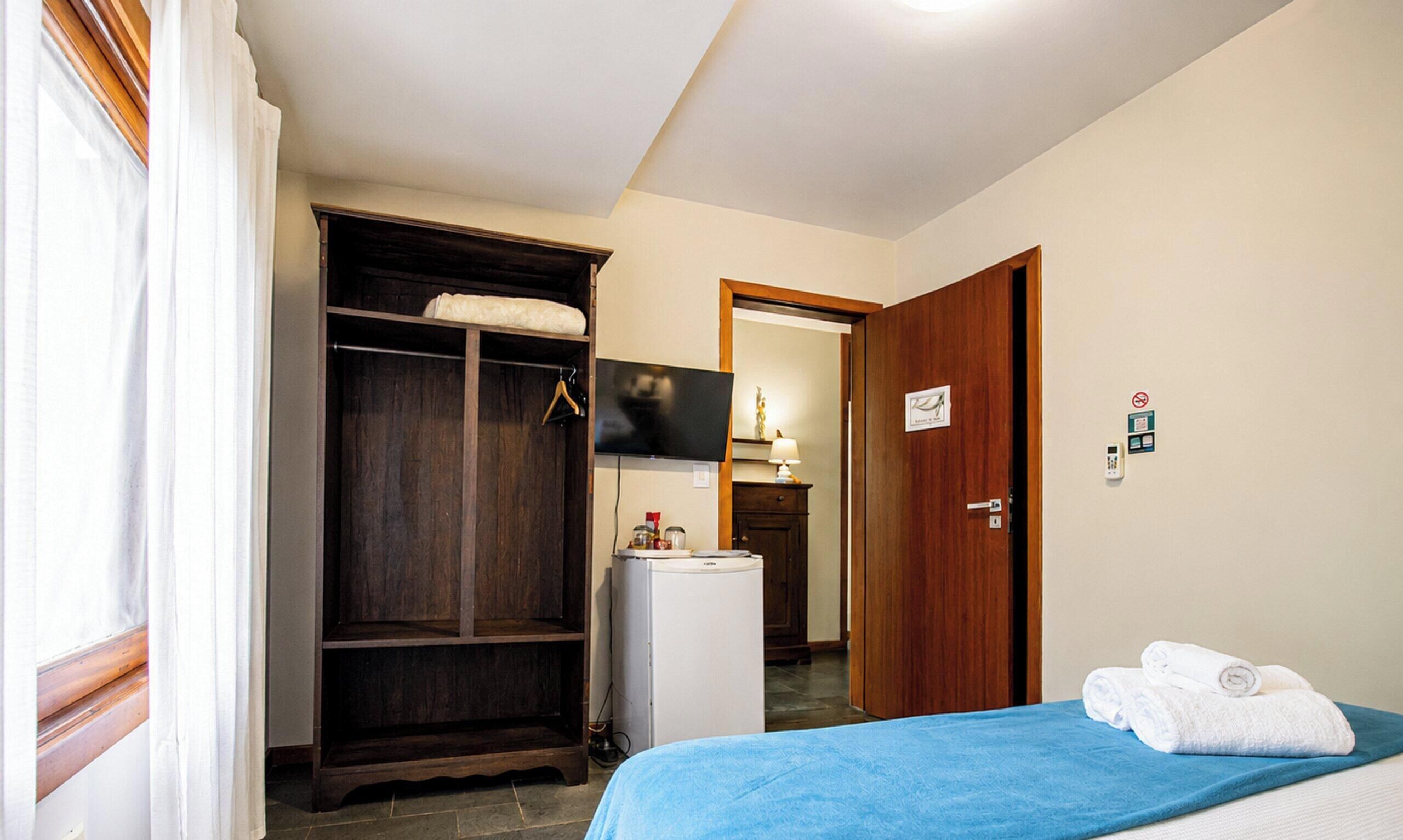 Una habitación de hotel con cama, armario, escritorio pequeño con lámpara, televisión y baño.