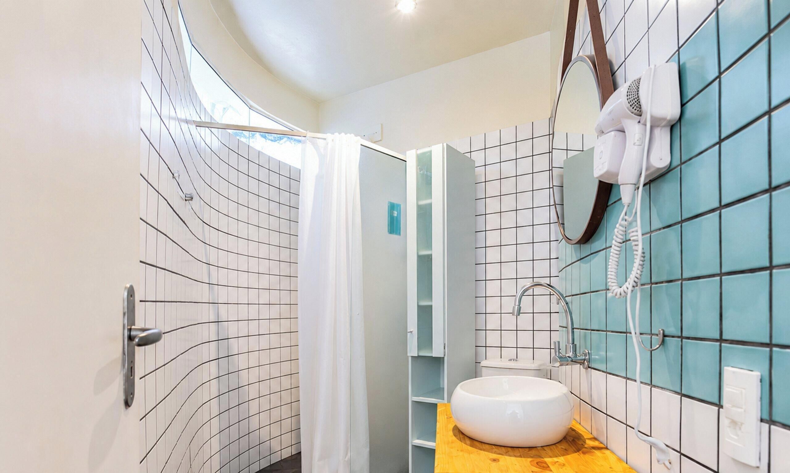 Un baño moderno con ducha de plato curva, un lavabo blanco y un secador de pelo montado en la pared.