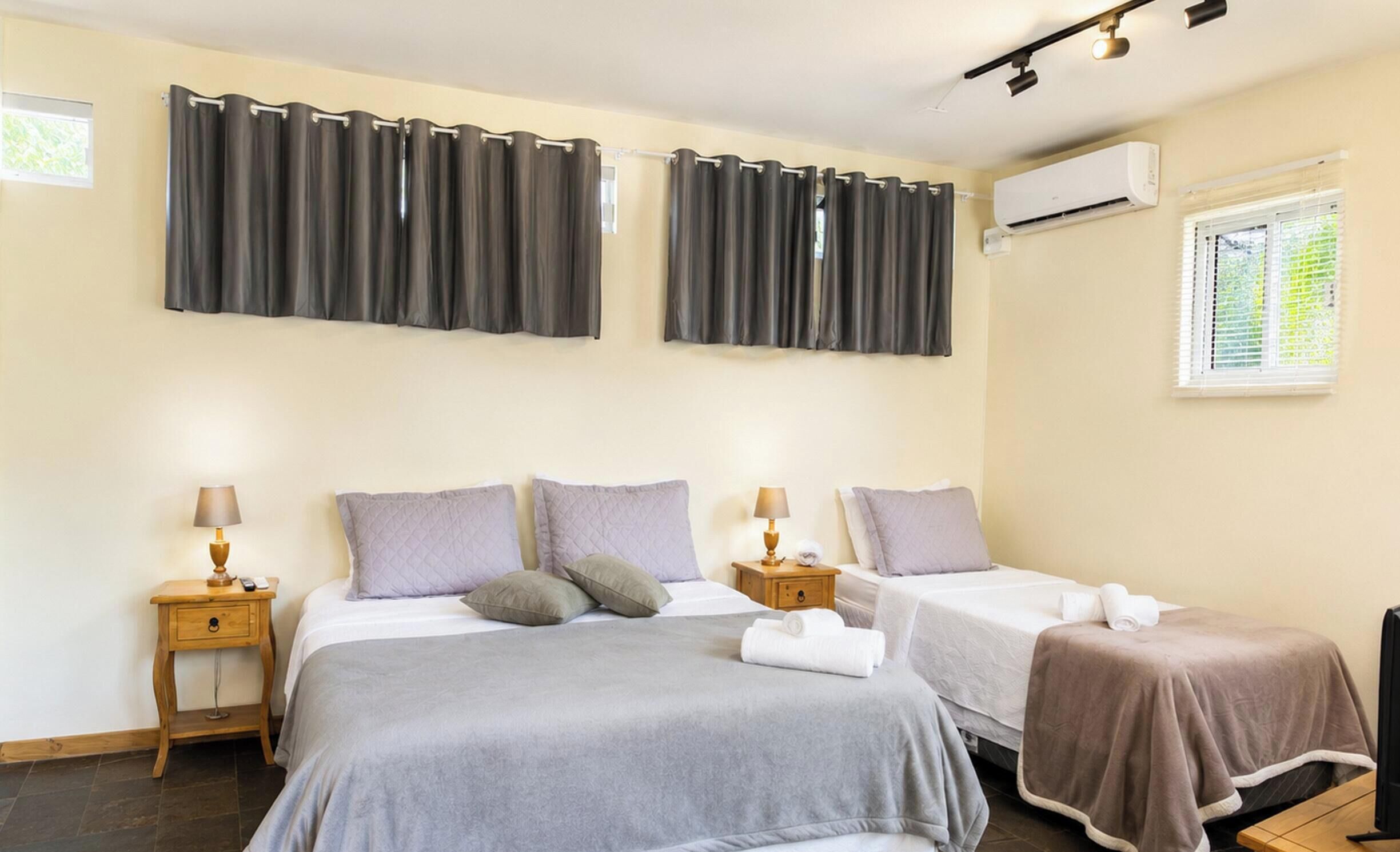 Habitación de hotel con dos camas, una ventana con persianas, un equipo de aire acondicionado y una mesita con lámpara.