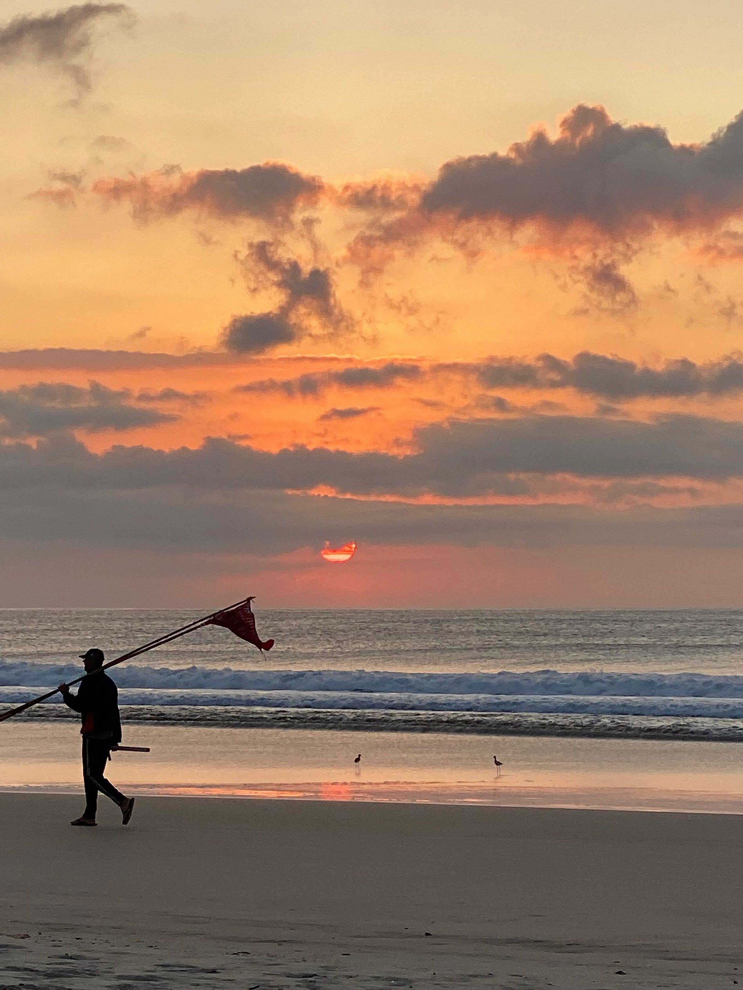 A beach scene with a person flying a kite near the water.