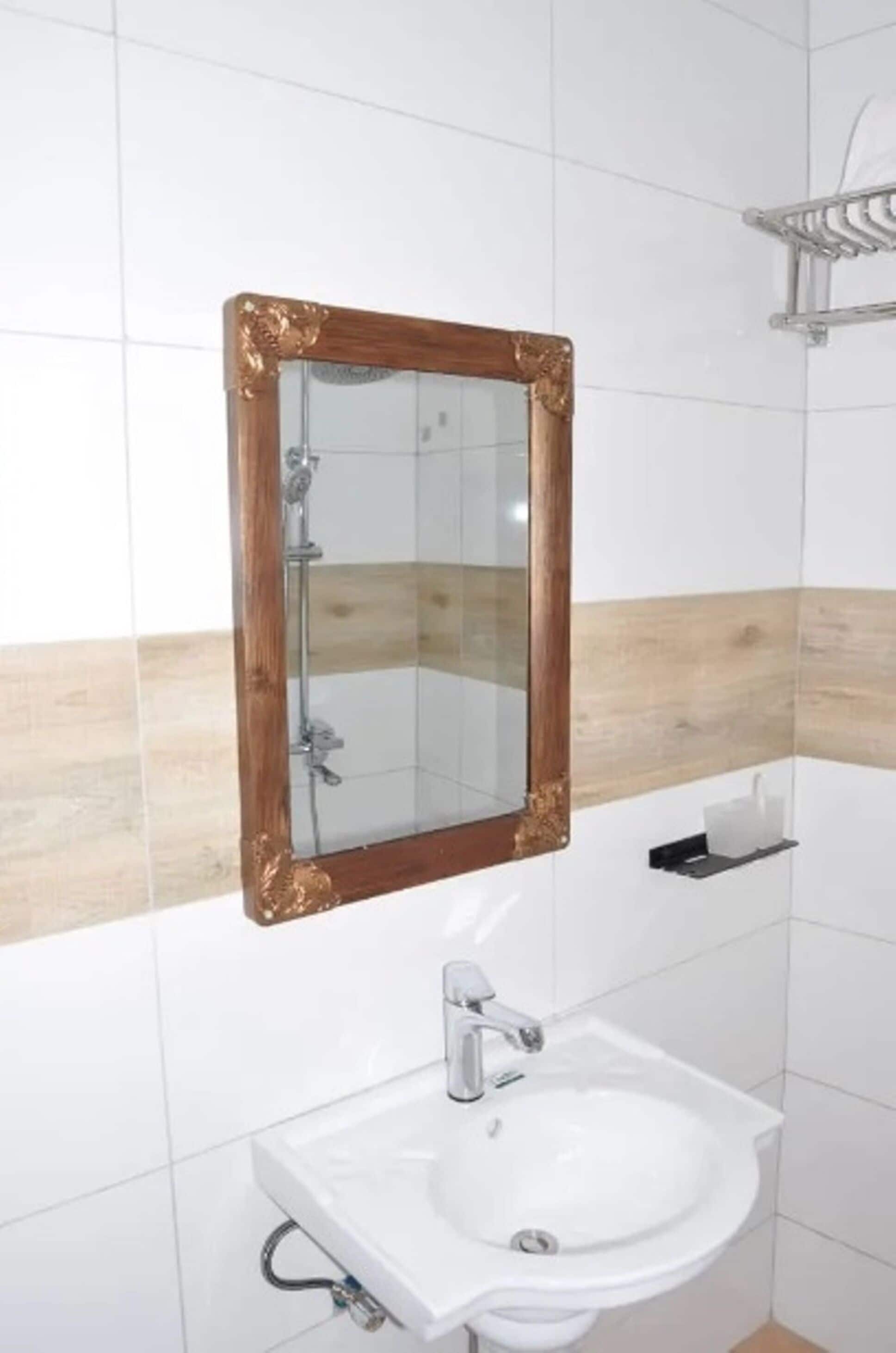 Un baño con un lavamanos blanco, un espejo con marco de madera y un perchero para toallas.
