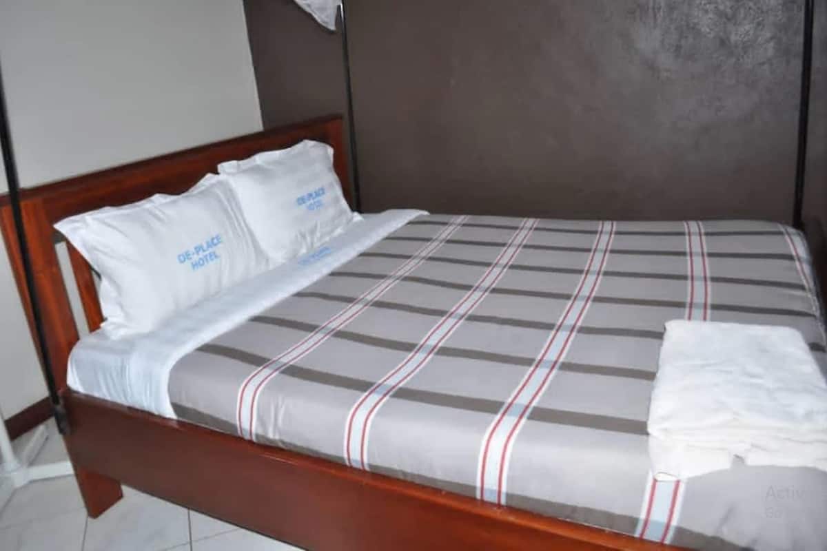 Una cama con colcha a rayas y almohadas blancas, cabecera de madera y pared lisa detrás.