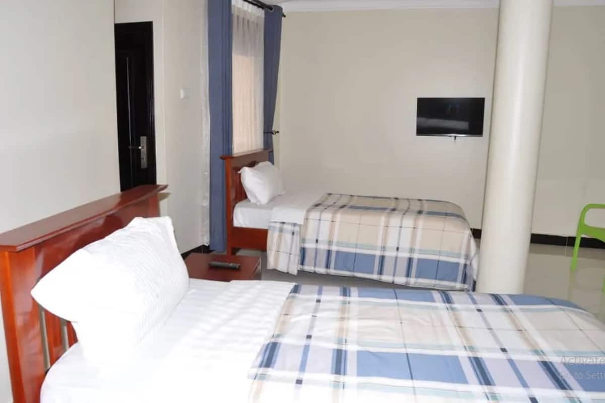 Habitación de hotel con una cama, una mesita de noche, un televisor montado en la pared y una silla verde.