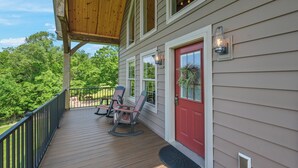 Une terrasse en bois avec deux fauteuils à bascule et une porte rouge, donnant sur un paysage verdoyant et luxuriant.