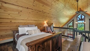 Une chambre à coucher en bois, avec un lit, une table de chevet, une lampe et une vue sur l’extérieur par une fenêtre.