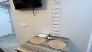 A dining area with a table, two woven placemats, a small potted plant, and a mounted flat-screen TV. - Executive Suite #2 with Parking (Pima County)