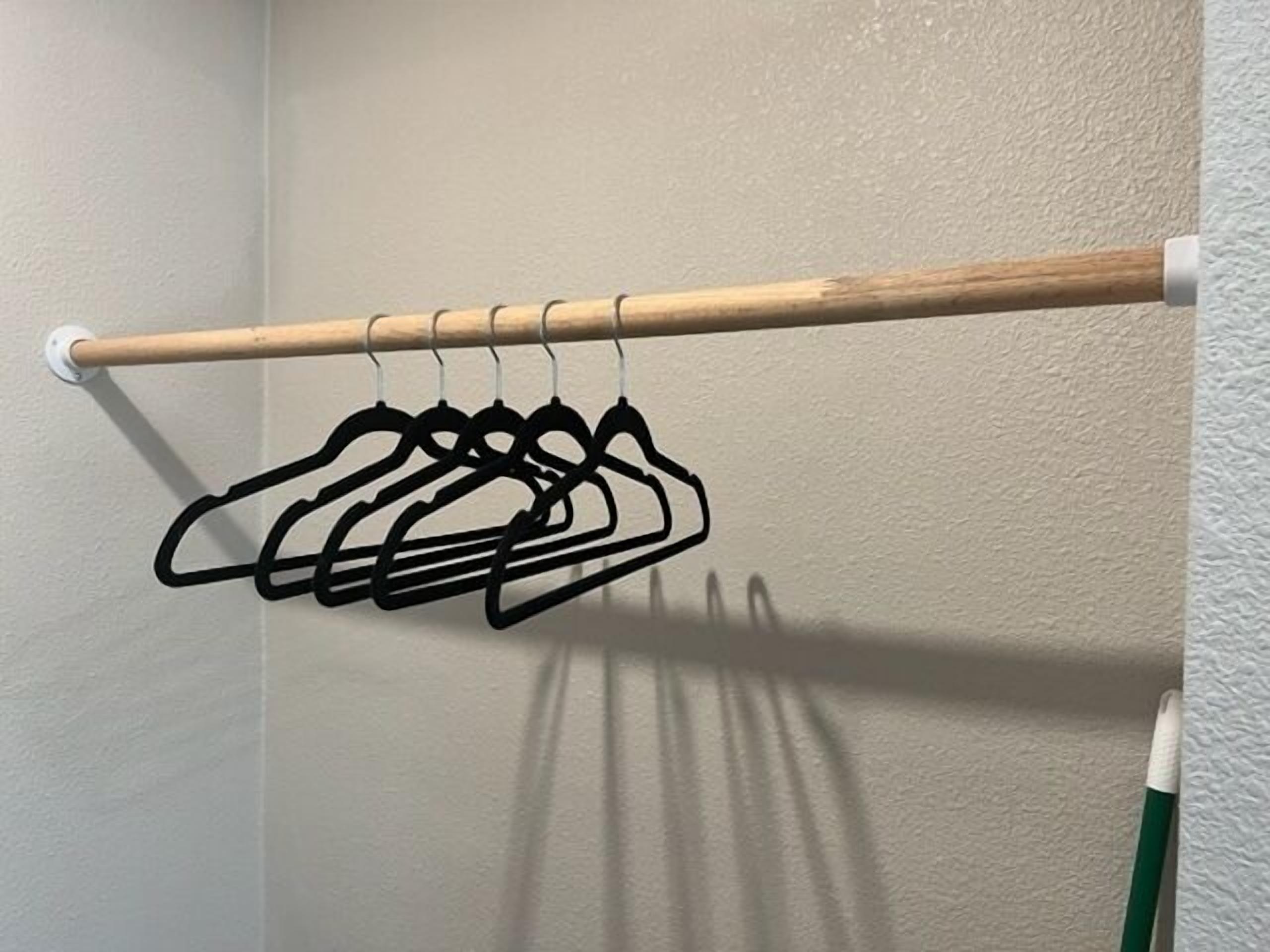 A wooden rod with black hangers against a textured wall.