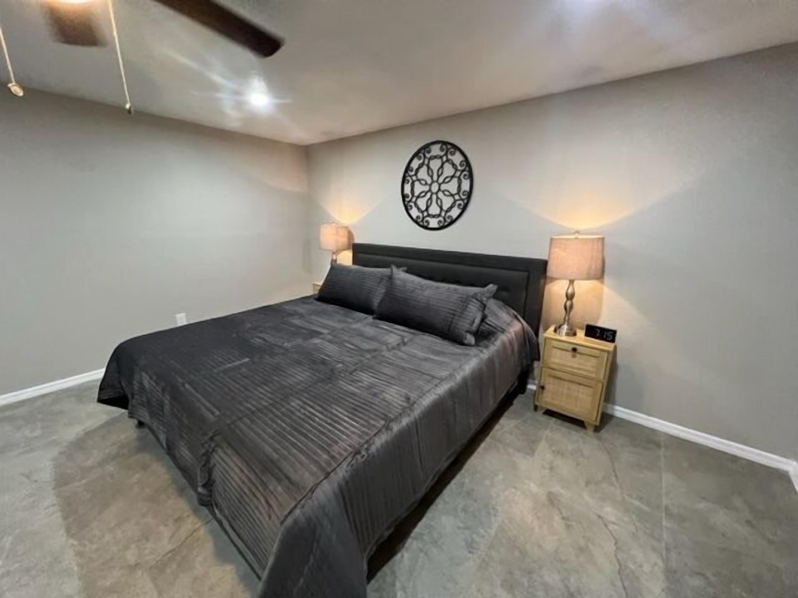 Ein modernes Schlafzimmer mit einem großen Bett, zwei Nachttischen mit Lampen, einem Deckenventilator und einer Wanddekoration.