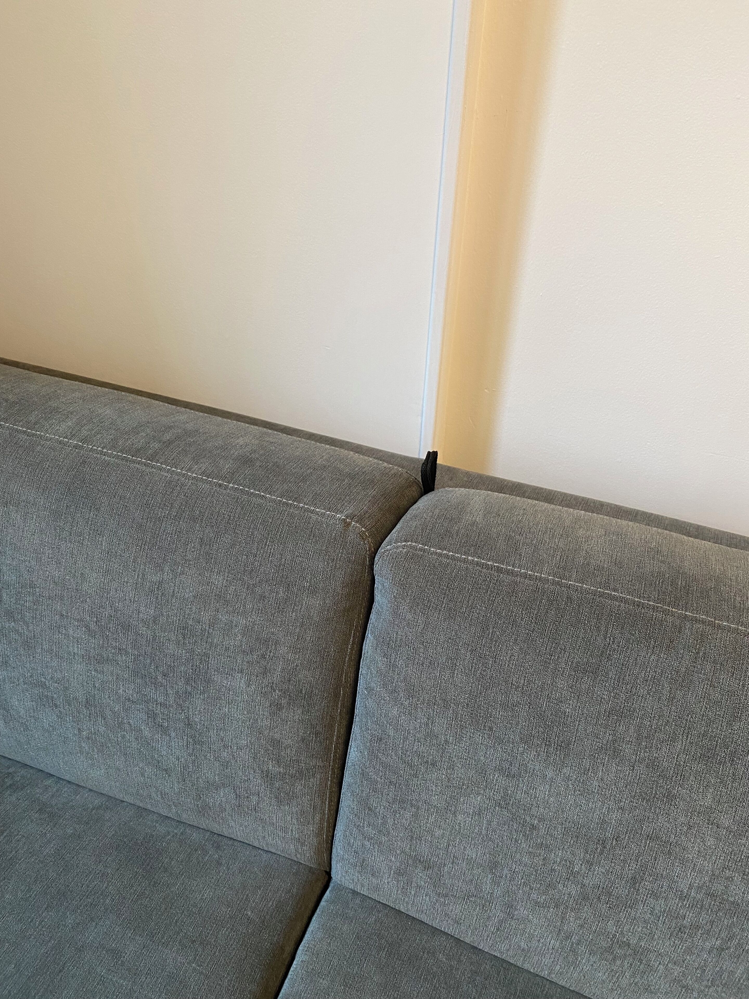 A grey sofa with a visible seam and a black object on the right side.