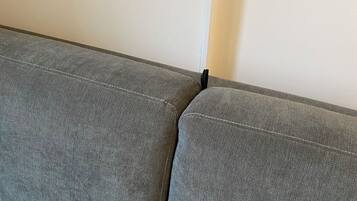 A grey sofa with a visible seam and a black object on the right side.
