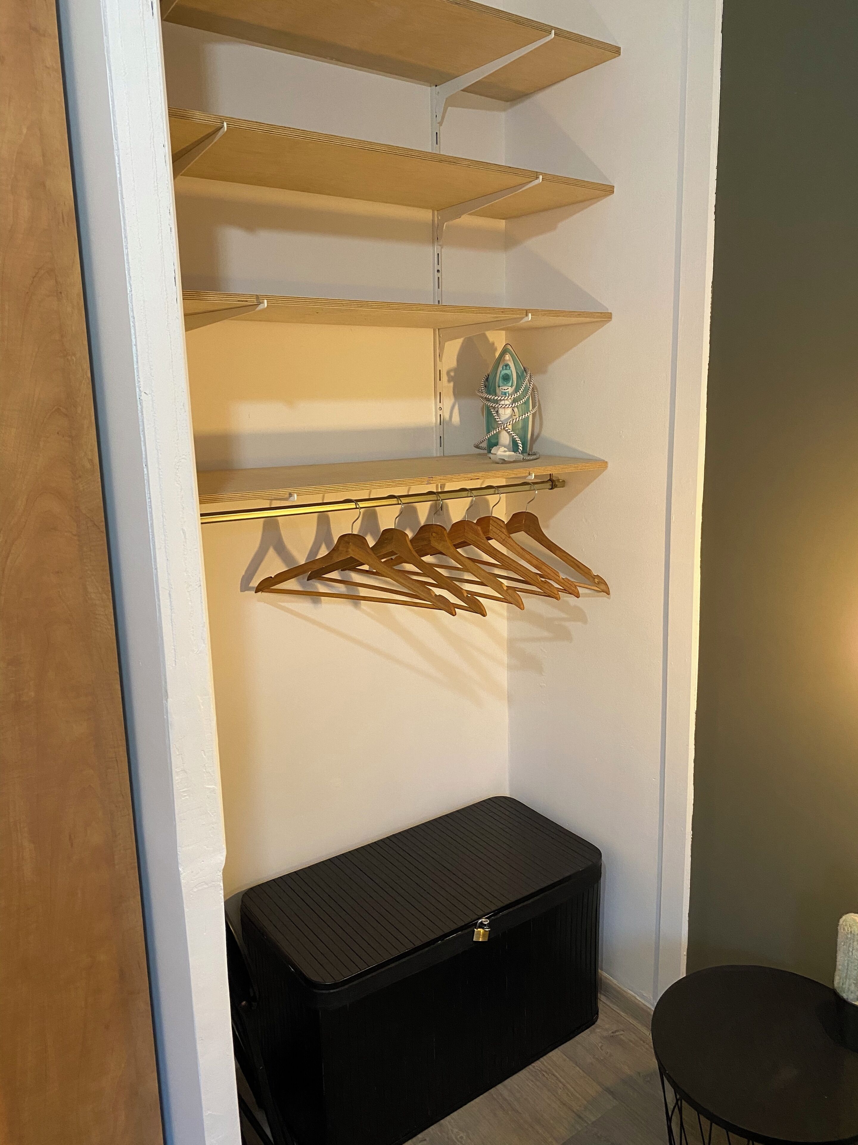 A storage closet with wooden shelves, a hanging rack, and a black storage box.
