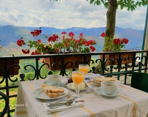 A table set with breakfast items including bread, butter, and orange juice, with a scenic mountain view in the background. - Vila Nazaré (Castro Daire)