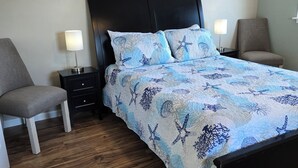 Una habitación de hotel con una cama, dos mesitas de noche, una silla y suelo de madera.
